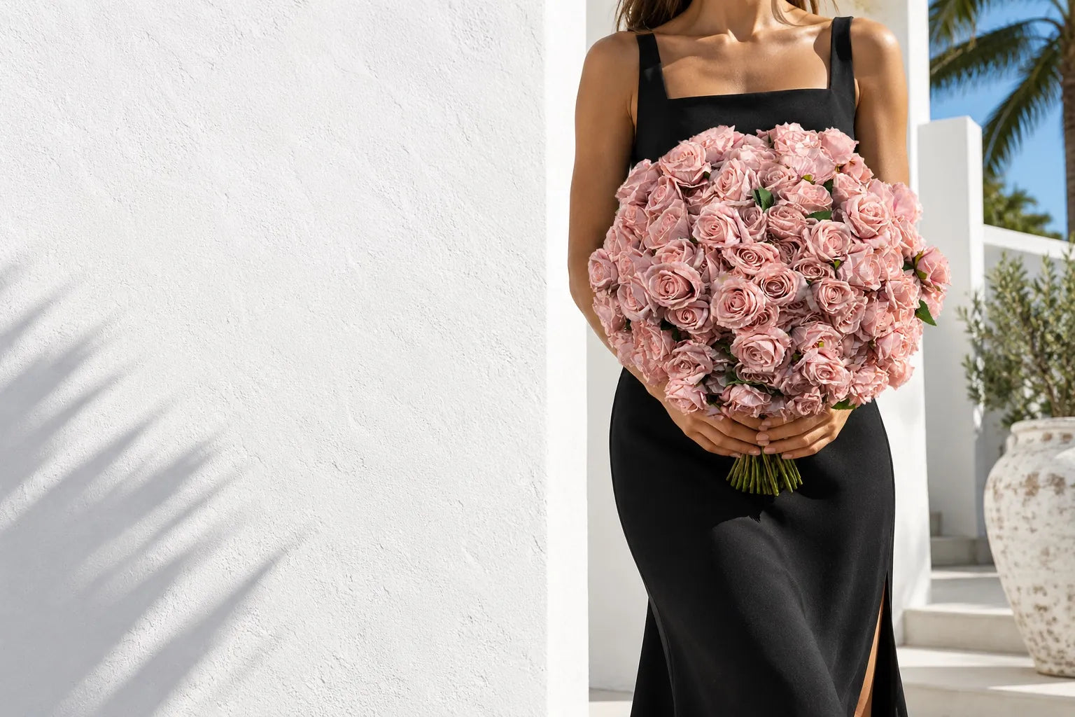 A woman in a black dress holding the pink Rose Bouquet, XL against a white wall