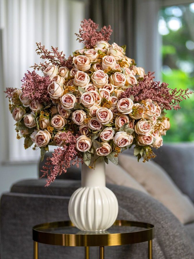 Blush roses in a white vase beside a living room sofa